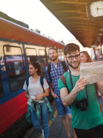 Personen mit einer Karte vor einem Zug | © Shutterstock / 501760414
