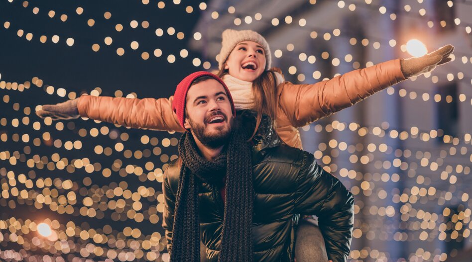 Weihnachtsmarkt Reisen mit railtour | © shutterstock / 1819607177 Glückliches Pärchen in Winterkleidung vor Weihnachtslichtern | © shutterstock / 1819607177