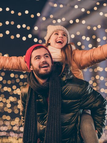 Glückliches Pärchen  in Winterkleidung vor Weihnachtslichtern | © shutterstock / 1819607177