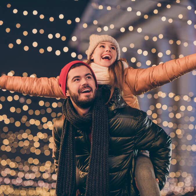 Glückliches Pärchen  in Winterkleidung vor Weihnachtslichtern | © shutterstock / 1819607177