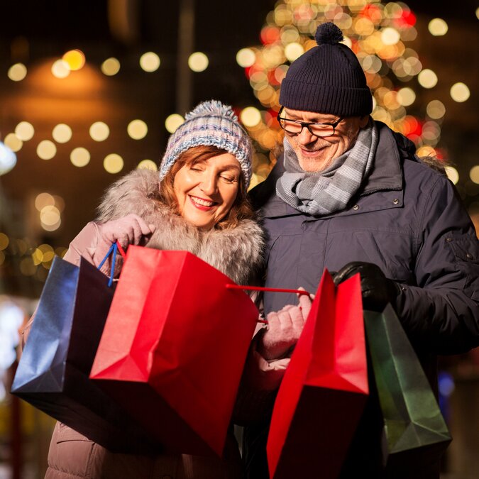 Glückliches Paar mit Einkaufstaschen am Weihnachtsmarkt nach erfolgreichem Weihnachtsshopping-Tag in der festlich geschmückten Stadt
 | © shutterstock / 1494691982