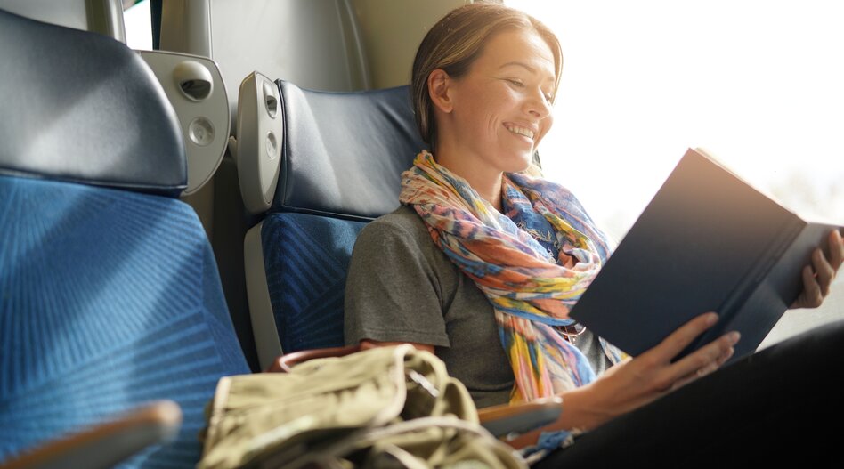 Person sitzt im Zug und liest ein Buch am Fenster. | © shutterstock_1210451854