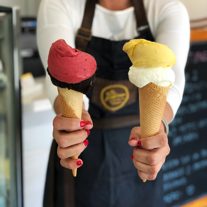 Zwei Eiswaffeln mit rosa und hellgelbem Glacé in der Hand einer Person | © La Golosa