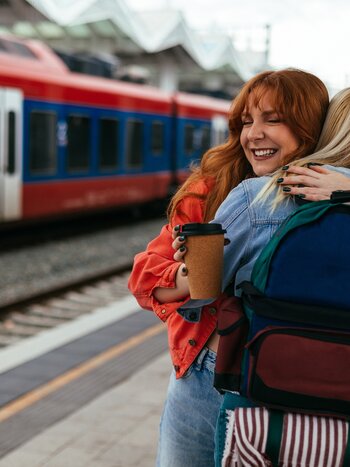 Zwei Personen umarmen sich am Bahnhof vor Zug | © shutterstock_2441467157