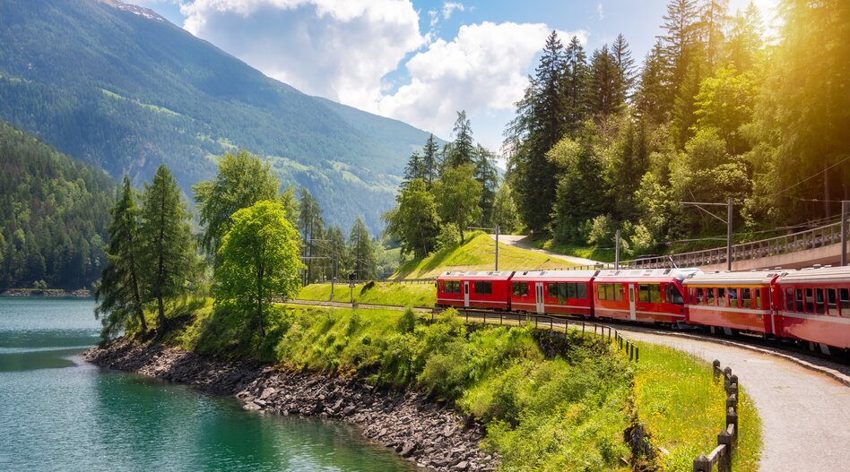 Ein roter Zug fährt an See entlang.