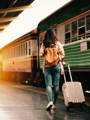 Frau mit Koffer auf Bahngleis vor grünem Zug