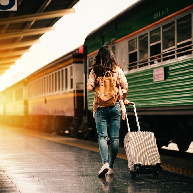 Woman with suitcase on railway track in front of green train