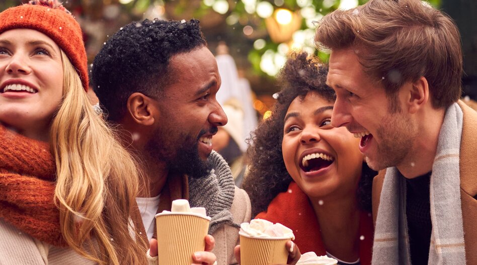 Four people holding takeaway cups in a festive winter setting | © shutterstock_2088780169