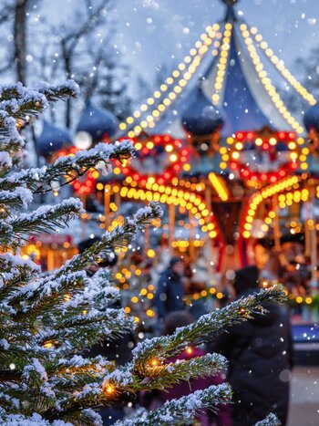 Illuminated carousel in Tivoli with a Christmas tree covered in snow in the foreground | © shutterstock / 2234281435