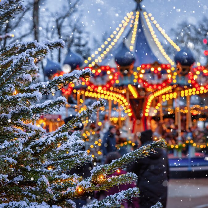 Beleuchtetes Karussell im Tivoli mit Christbaum voller Schnee im Vordergrund | © shutterstock / 2234281435