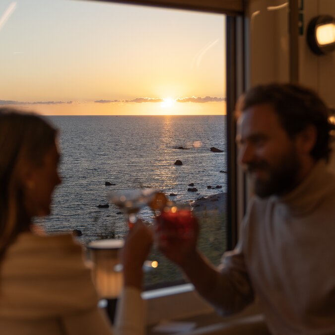 La Dolce Vita Orient Express - Couple enjoying a drink by the window with sunset in the background. | © La Dolce Vita Orient Express