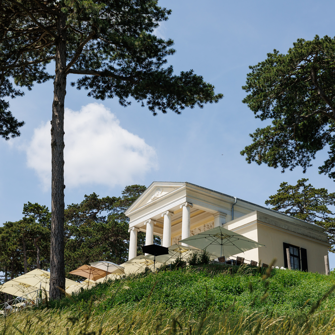 La Gloriette de style néoclassique se dresse sur une colline dans le parc du château d’Eisenstadt, dans le Burgenland. Entouré de grands pins et d’espaces verts aménagés, ce bâtiment historique constitue un remarquable point de vue. | © Eisenstadt2026_0042©BurgenlandTourismus_MariaHollunder