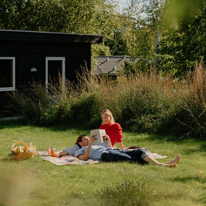 Zwei Personen entspannen auf einer Decke im Garten eines Ferienhauses in Dänemark und lesen im Grünen. | © Daniel Overbeck