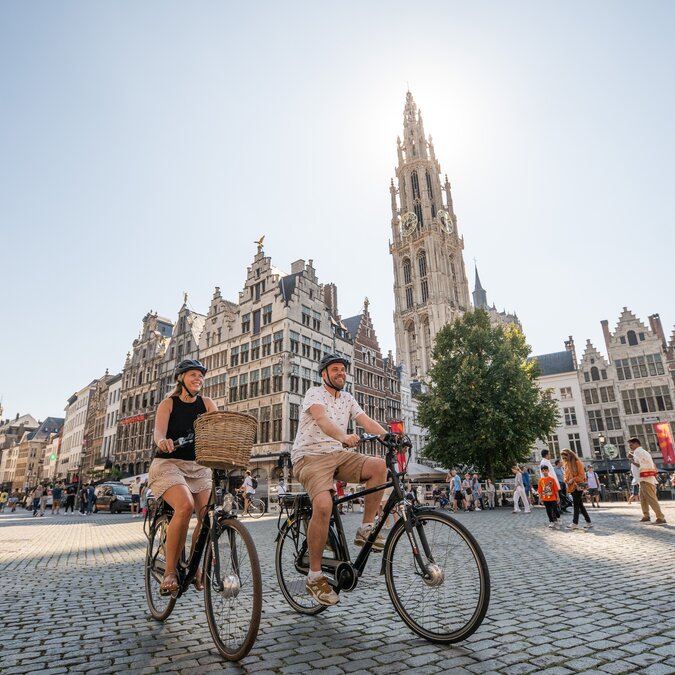 Cyclistes sur la Grand-Place d'Anvers devant les maisons à pignons flamandes et la tour de la cathédrale Notre-Dame. | © Piet de Kersgieter – Anvers Grote Markt