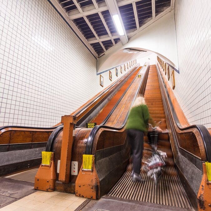 Escaliers roulants historiques en bois dans le tunnel Sint-Anna à Anvers avec une personne et un vélo. | © Piet de Kersgieter –  Vlaeykensgang Centre d'Anvers