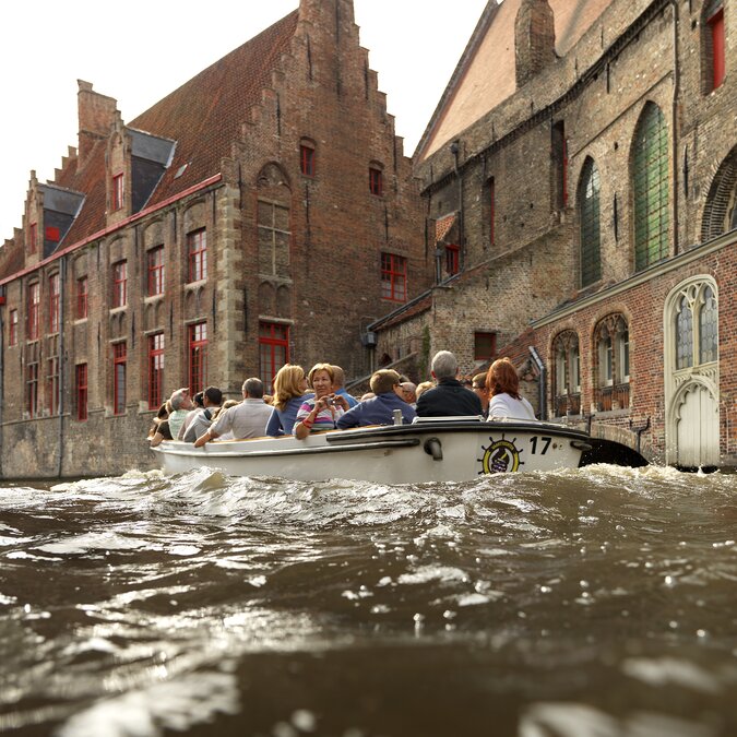 Bateau avec des visiteurs sur le canal à Bruges, entouré de maisons médiévales en briques. | ©  Visit Brugge – Promenade en bateau