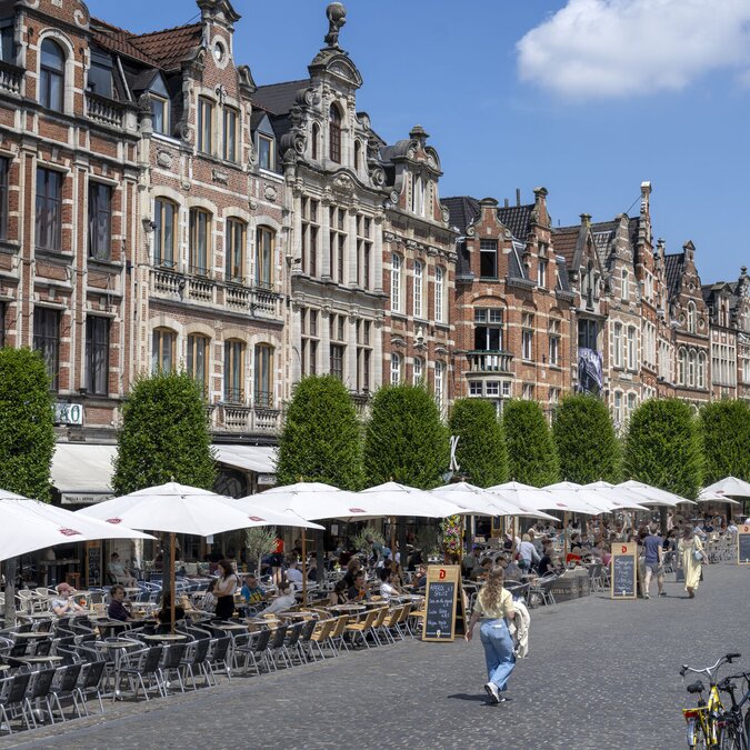 Une place animée à Louvain, avec ses façades historiques en briques, ses rangées d'arbres bien entretenues et ses nombreuses terrasses de café ornées de parasols. | © Karl Bruninx