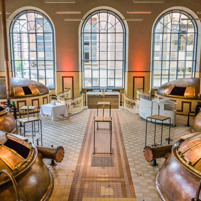 Intérieur d'une brasserie historique à Louvain, avec de grandes cuves de brassage en cuivre, de hautes fenêtres en arc et un sol carrelé clair. | © Stad Leuven