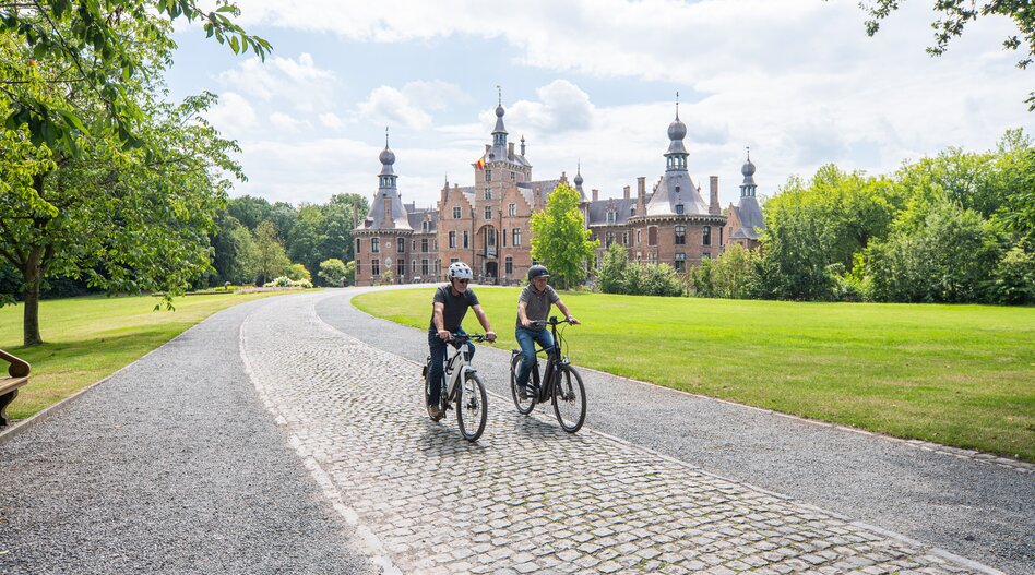Cyclistes en route vers le château d'Ooidonk sur une allée pavée dans un parc verdoyant. | © Piet de Kersgieter – Kasteel Ooidonk