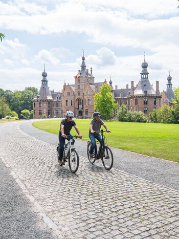 Radfahrer auf dem Weg zum Schloss Ooidonk über eine Kopfsteinpflasterallee in grüner Parklandschaft. | © Piet de Kersgieter – Kasteel Ooidonk