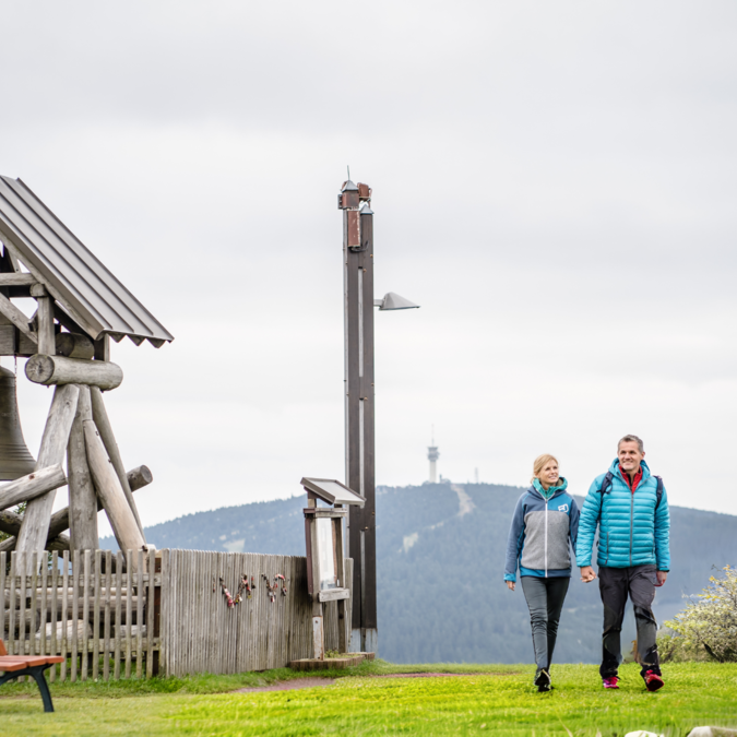 Deux personnes marchant près d’une grande cloche en bois | © TMGS Dennis Stratmann