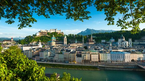 Weitläufige Aussicht über die Salzburger Altstadt mit der Salzach, barocken Kirchtürmen und der Festung Hohensalzburg, eingerahmt von grünen Blättern und Hügeln im Hintergrund. | &copy; Tourismus Salzburg GmbH, Guenter Breitegger