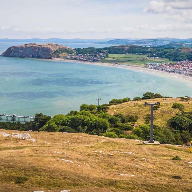 Vue de Llandudno au Pays de Galles avec une baie aux courbes harmonieuses, une longue plage de sable, une jetée et une ville côtière au pied d’un paysage vallonné. | © Crown Copyright (2026) Welsh Government