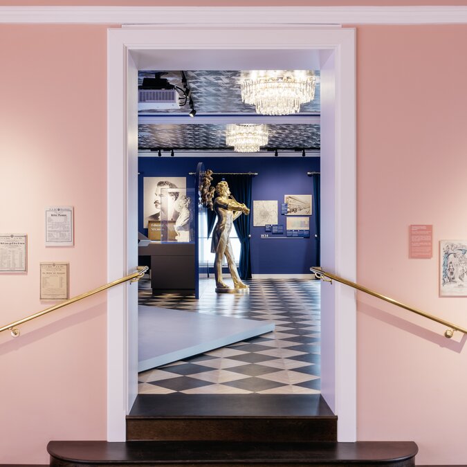 Blick durch einen rosafarbenen Eingangsbereich in einen Ausstellungsraum mit Skulpturen und historischen Exponaten. | © Wien Tourismus |Gregor Hofbauer