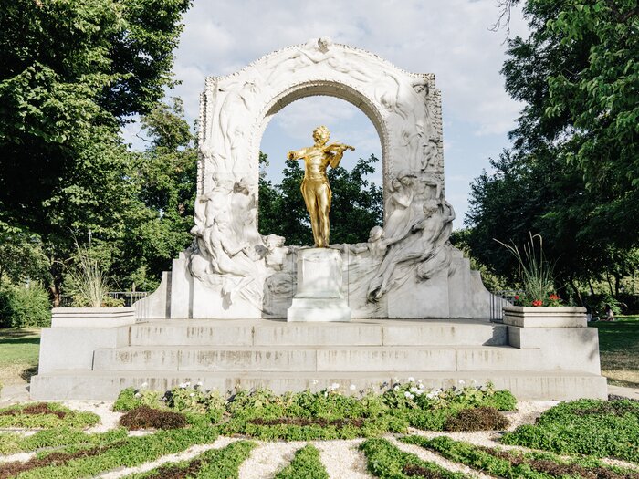 The golden statue of Johann Strauss II stands in Vienna's Stadtpark under an ornately decorated white marble arch. | © Wien Tourismus | Gregor Hofbauer