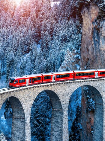 Aerial view of the train through the famous mountain in Filisur, Switzerland. Train Express in the Swiss Alps snow winter landscape. | © Shutterstock 2256994783