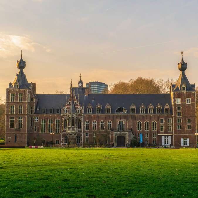 Historisches Schloss Arenberg in Leuven, aufgenommen bei warmem Abendlicht, mit grosser Grünfläche im Vordergrund und Bäumen im Hintergrund. | © Shutterstock 2305351959