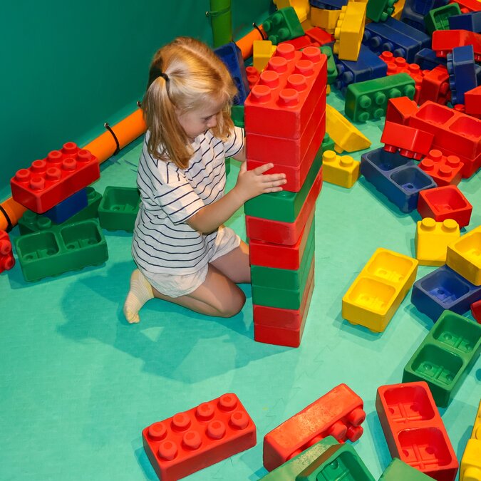 Ein Mädchen spielt auf dem Boden mit verschiedenfarbigen Legosteinen. | © shutterstock / 2503988239