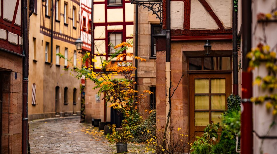 Schmale Kopfsteinpflasterallee mit historischen Fachwerkhäusern und Herbstblättern schaffen eine warme mittelalterliche Atmosphäre | © Natalia Schuchardt