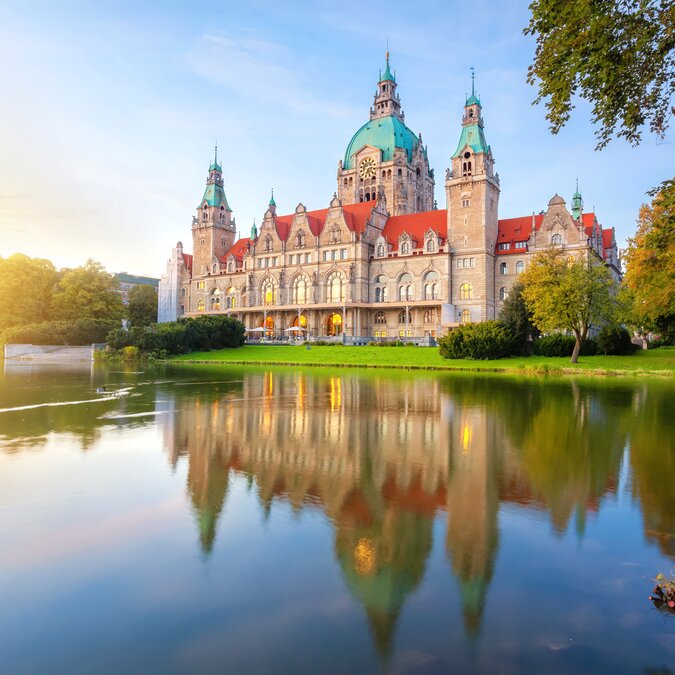 Neuer Rathaus in Hannover, der bei Sonnenuntergang im Wasser reflektiert | © Shutterstock 1876052881