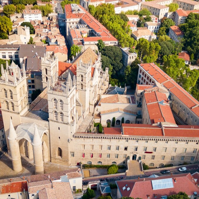 Aerial view of the Saint-Pierre Cathedral in Montpellier, surrounded by historic buildings with red tile roofs and lush greenery, defining the old town. | © shutterstock / 2526562201