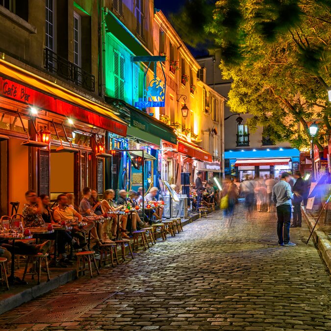 Typischer nächtlicher Ausblick auf die gemütliche Strasse mit Tischen für Cafés und Strassenkünstler im Viertel Montmartre in Paris, Frankreich | © Shutterstock 2043692486