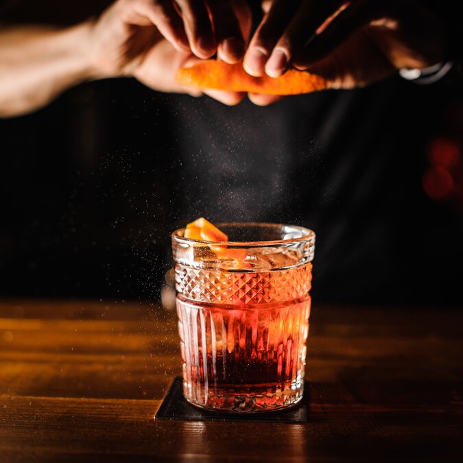 Bartender with cocktail and orange peel preparing cocktail at the bar. | © Shutterstock 711382402