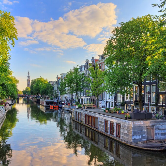 Péniches sur le canal Prinsengracht, classé au patrimoine mondial de l'UNESCO, avec la Westerkerk (église occidentale), un matin d'été avec ciel bleu et nuages et reflet dans les miroirs à Amsterdam, Pays-Bas | © Shutterstock 608658164