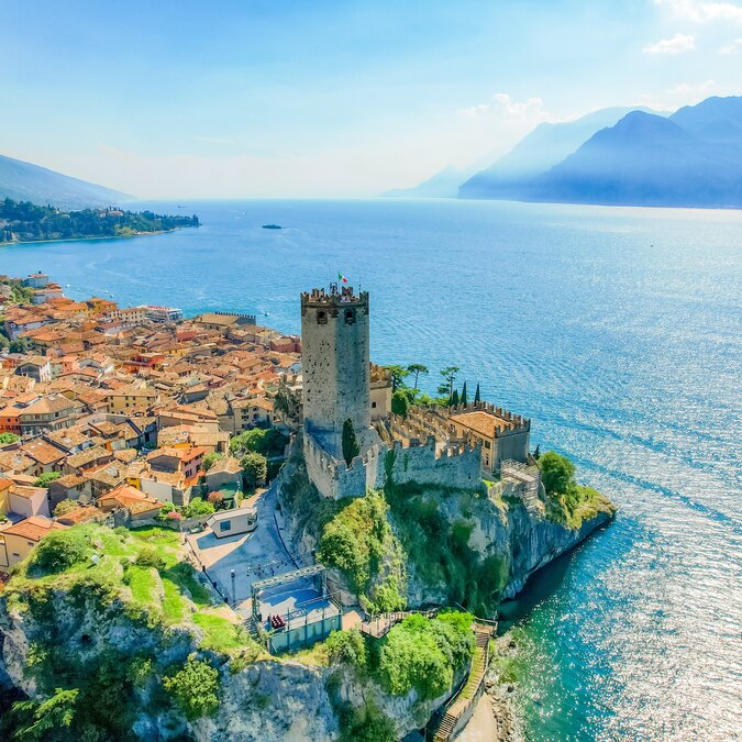 Luftaufnahme vom Scalinger Castle und der Altstadt von Malcesine direkt am Ufer des Gardasees und Berge im Hintergrund | © shutterstock / 2498491379