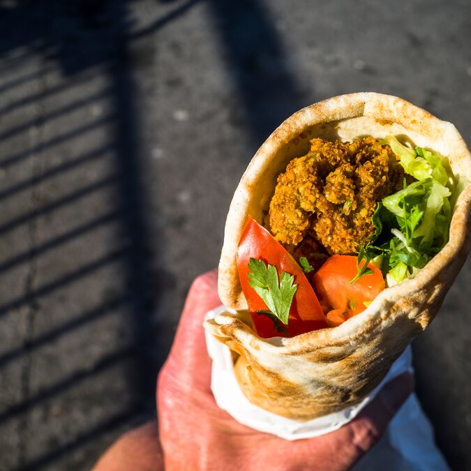 Rolled falafel in the hand of a street market visitor in Stockholm | © shutterstock / 1992336137