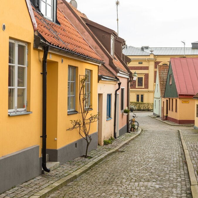 Charmante schmale Strasse mit bunten kleinen Häusern und Kopfsteinpflaster in Ystad, Schweden | © shutterstock_2622377935